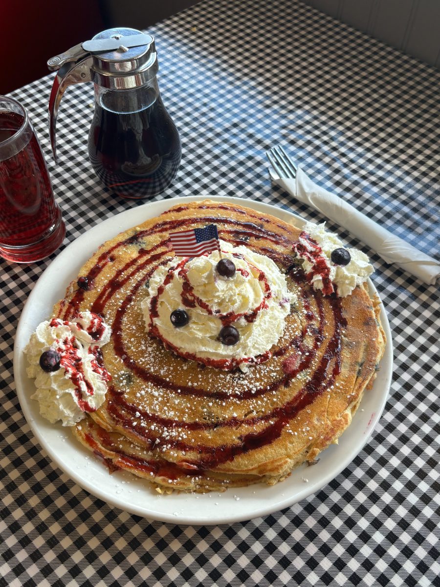 A giant blueberry pancake with whipped cream and blueberry sauce on a checkered table