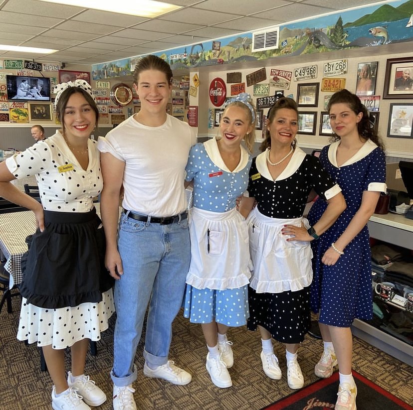 The Jimmy's crew in polka-dot diner dresses and aprons smiling inside the restaurant